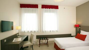 A hotel room with two beds, a desk, a chair, a TV, and a window with curtains.