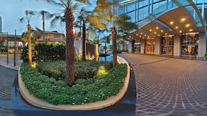 A modern hotel entrance with a curved glass facade, a landscaped garden with palm trees, and a paved walkway. - Marriott Executive Apartments Bangkok, Sukhumvit Thonglor (Bangkok)