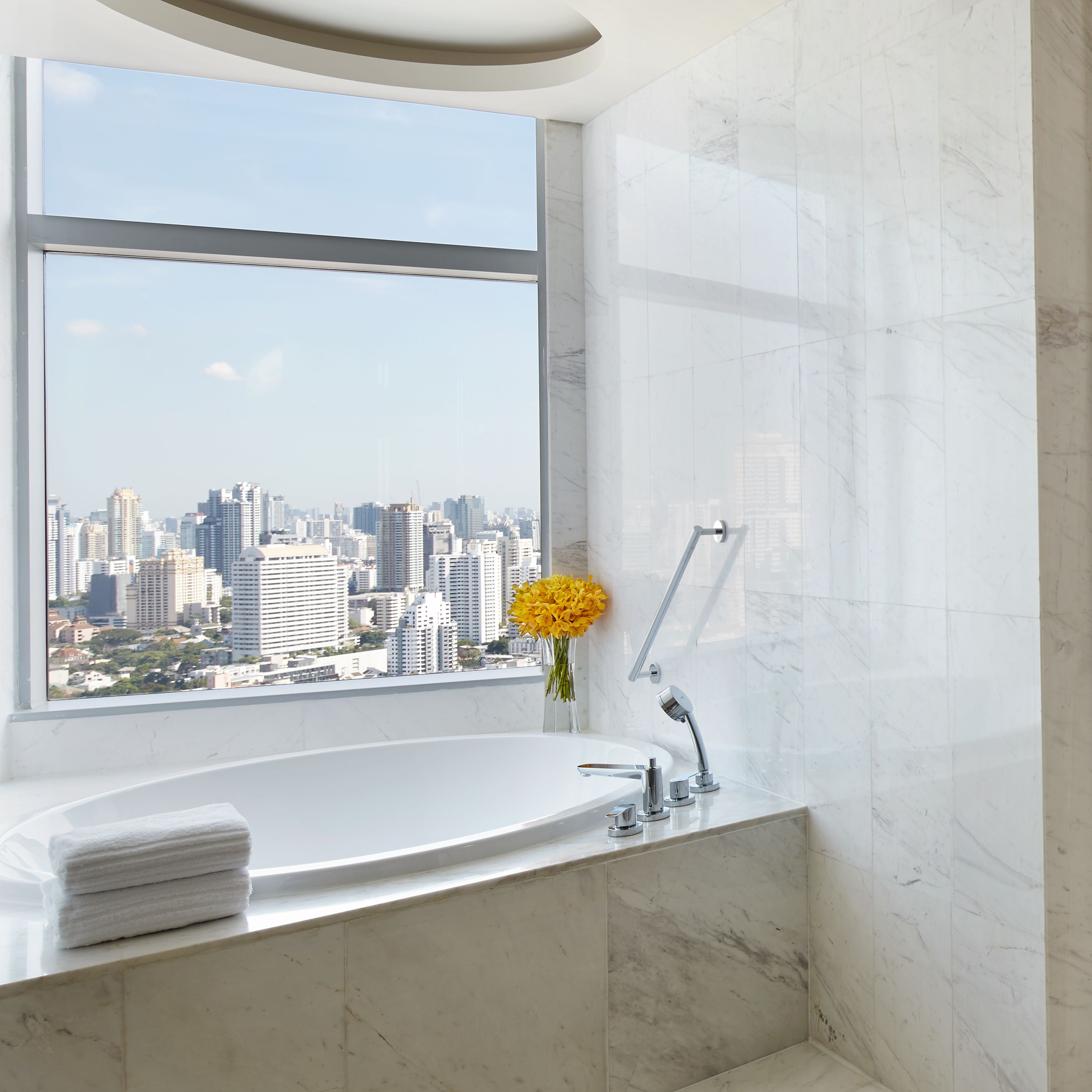 A modern bathroom with a large window, a bathtub, and a city view.