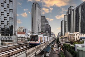 Un moderno edificio de gran altura con fachada curva, un tren pasando por una vía elevada y una calle concurrida abajo.