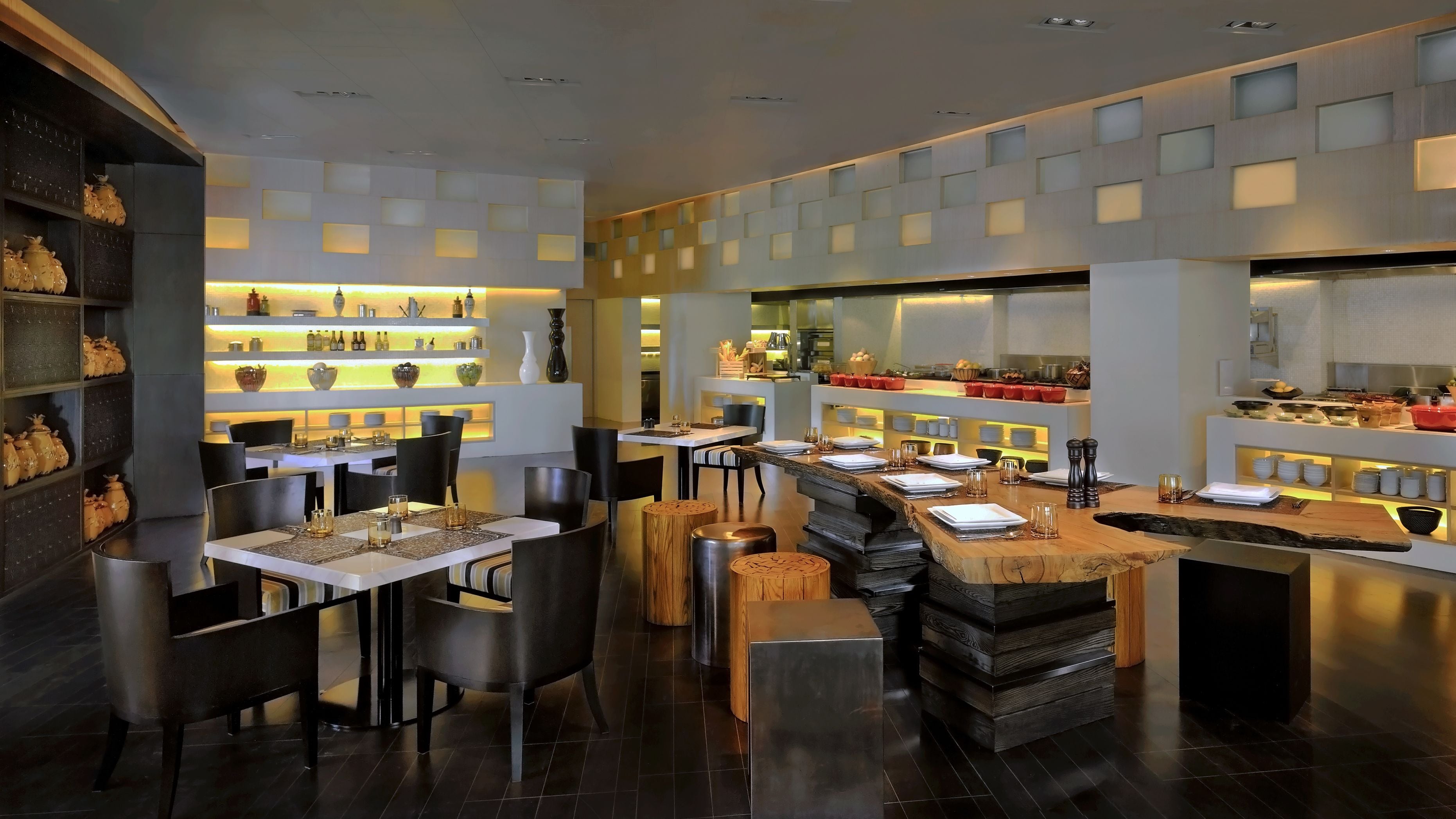 Ein modernes Restaurantambiente mit mehreren Tischen, Stühlen und einer im Hintergrund sichtbaren Küche.