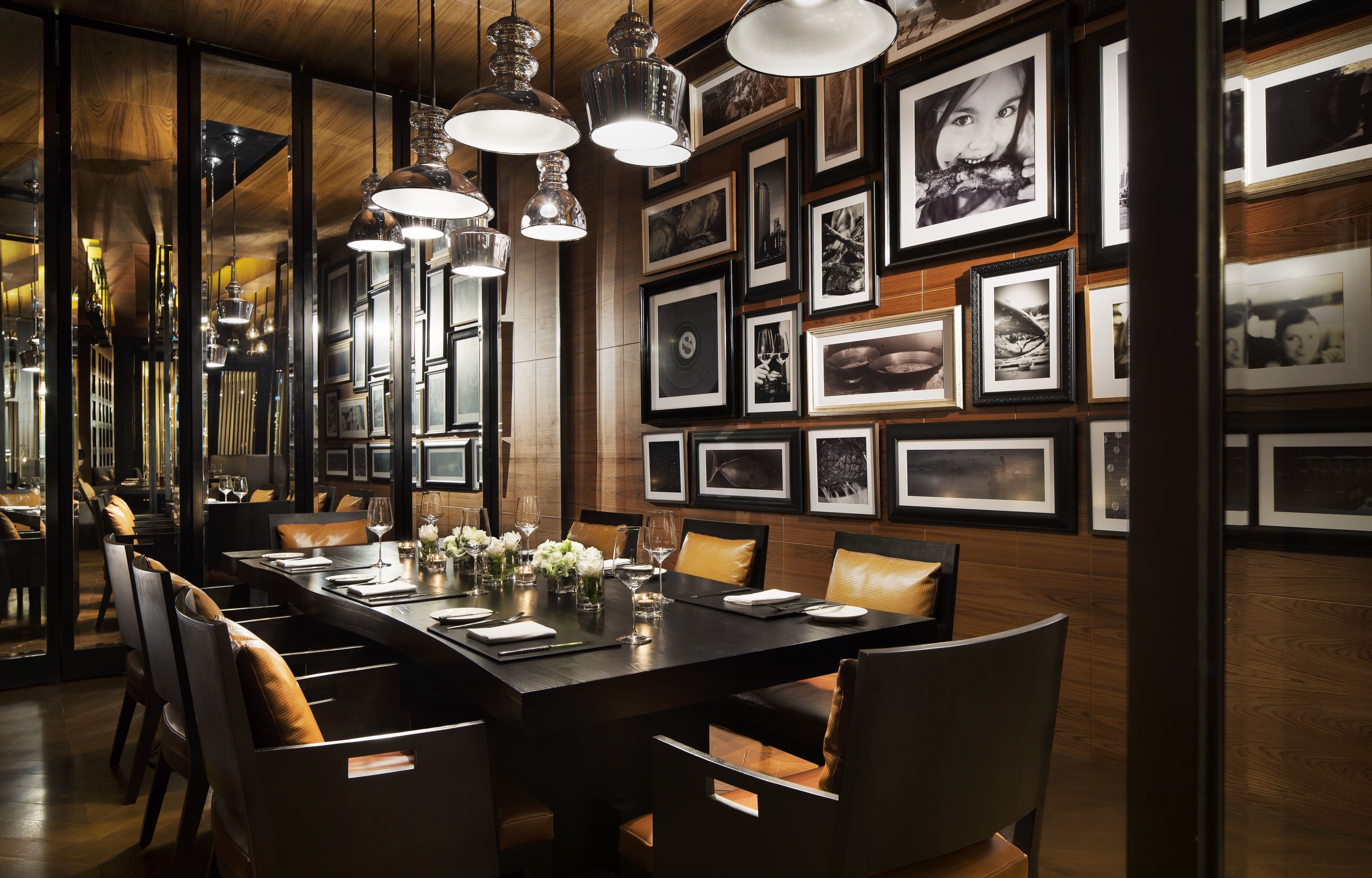A dining area with a long table set for six, surrounded by chairs. The walls are adorned with framed photographs.