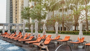 A poolside area with lounge chairs and umbrellas, a pool, and tall buildings in the background. - Marriott Bangkok Sukhumvit (Bangkok)