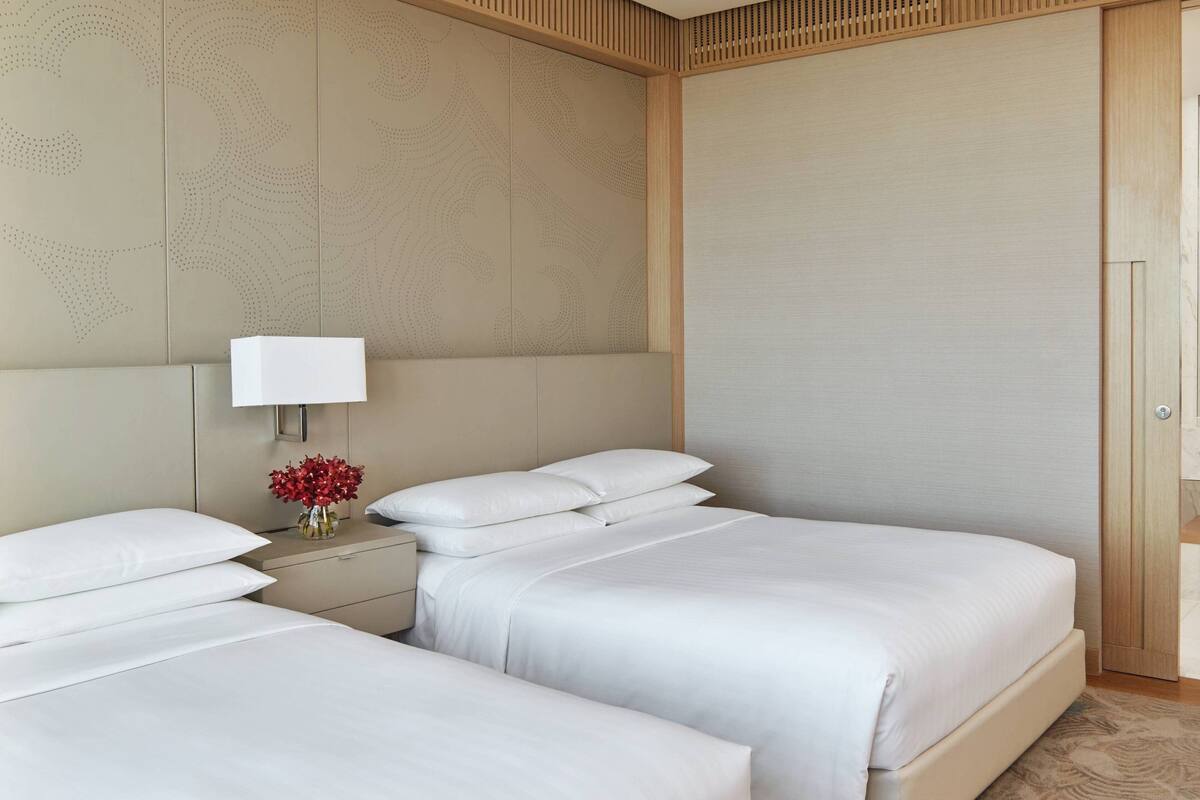 Una habitación de hotel con dos camas, una mesita de noche con lámpara y un jarrón con flores.