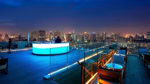 Un bar en la azotea con barra circular, asientos y vista al horizonte de la ciudad.
