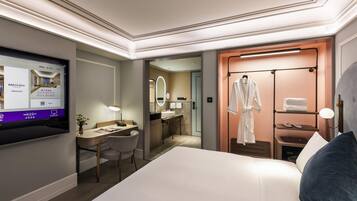 A hotel room with a bed, desk, chair, robe rack, and a TV displaying hotel information.
