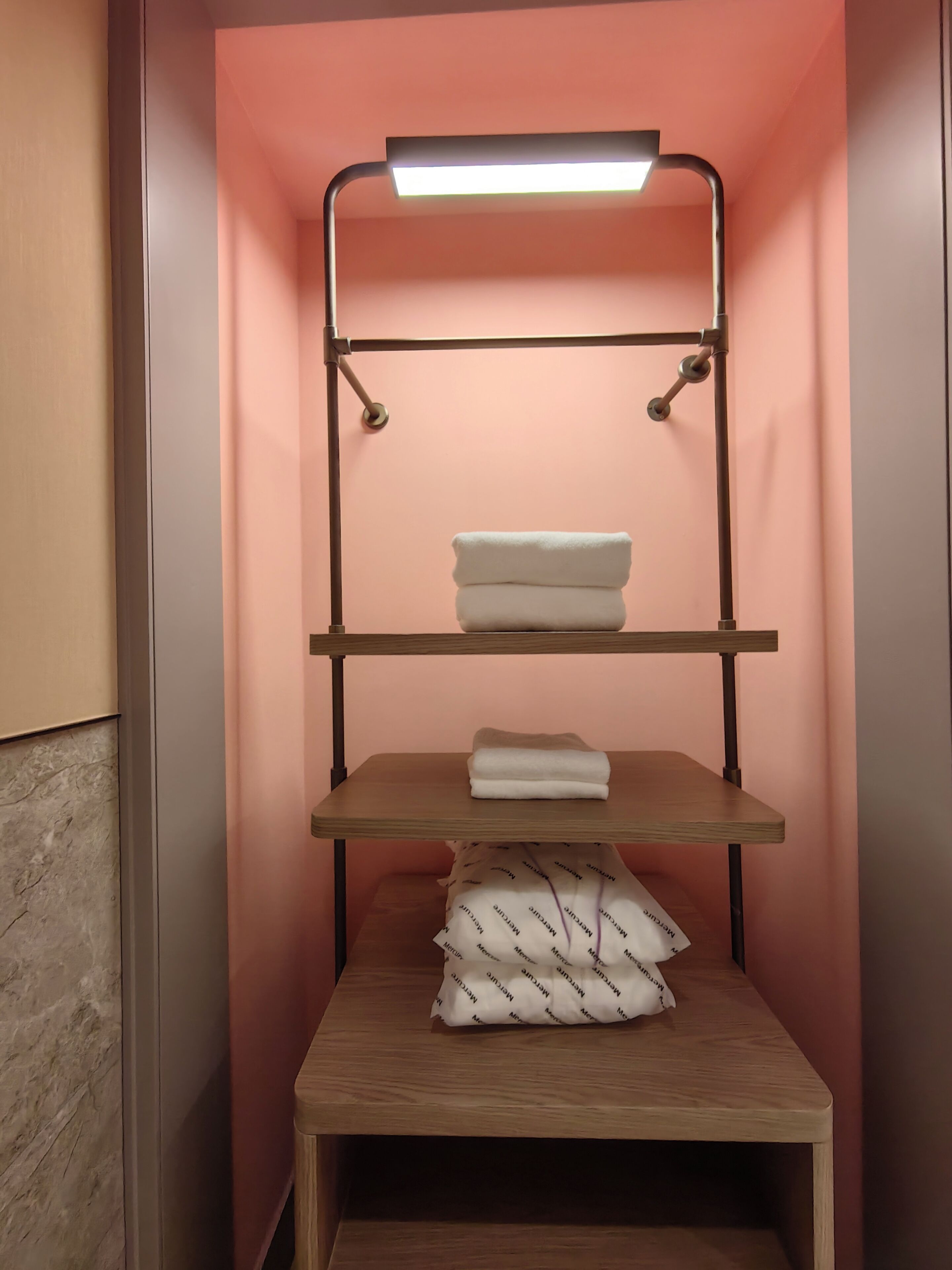 Une étagère murale, avec un luminaire placé au-dessus, servant à ranger des serviettes pliées et un sac à motifs.