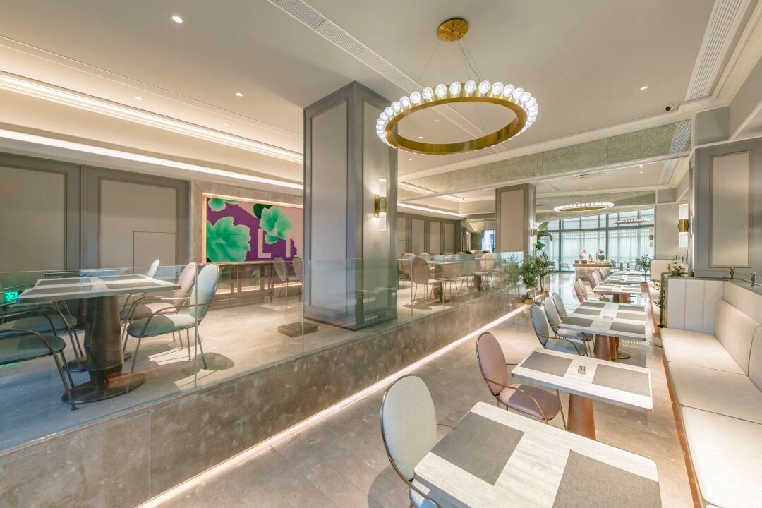 A modern hotel lobby with a central seating area, glass partitions, and a large window providing natural light.