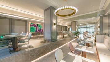 A modern hotel lobby with a central seating area, glass partitions, and a large window providing natural light.