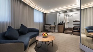 Una habitación de hotel moderna con sofá, una mesa redonda de centro con fruta, un escritorio y un vestidor.