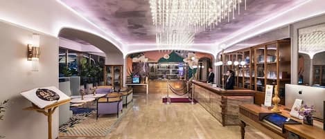 A hotel lobby with a reception desk, seating area, and a large chandelier.
