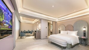 Una habitación de hotel moderna con una cama grande, una zona de estar con sofá y sillones, un escritorio pequeño y un televisor.