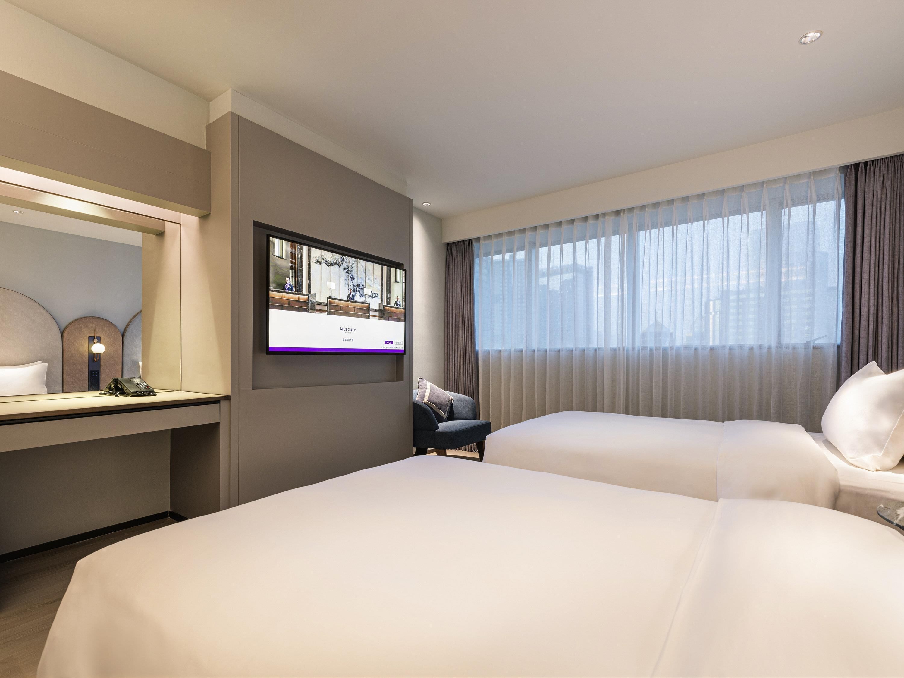 Habitación de hotel con dos camas, un escritorio con teléfono, televisor en la pared y ventana con cortinas.