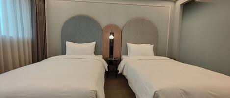 A hotel room with two beds, a wooden floor, a nightstand, and a wall-mounted light fixture.