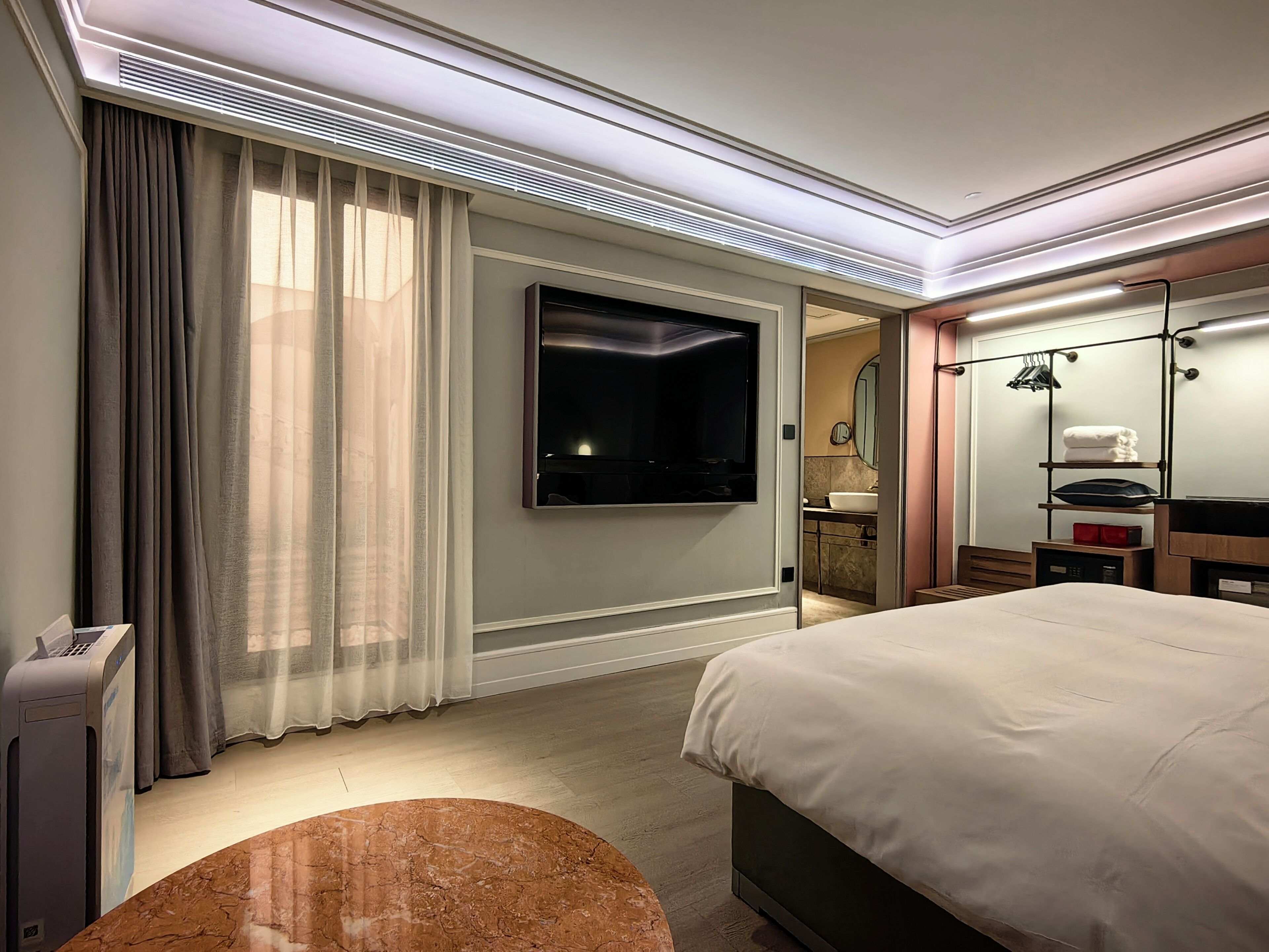 Une chambre d’hôtel comprenant un lit, un téléviseur fixé au mur, une salle de bain avec un lavabo et un miroir, et un plafond doté d’un éclairage encastré.