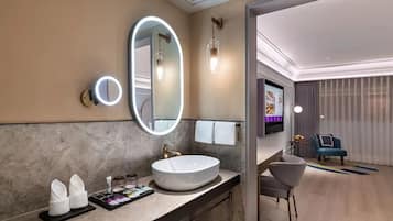 Un baño moderno con un lavamanos ovalado grande, un espejo redondo con luz y un televisor de pantalla plana.