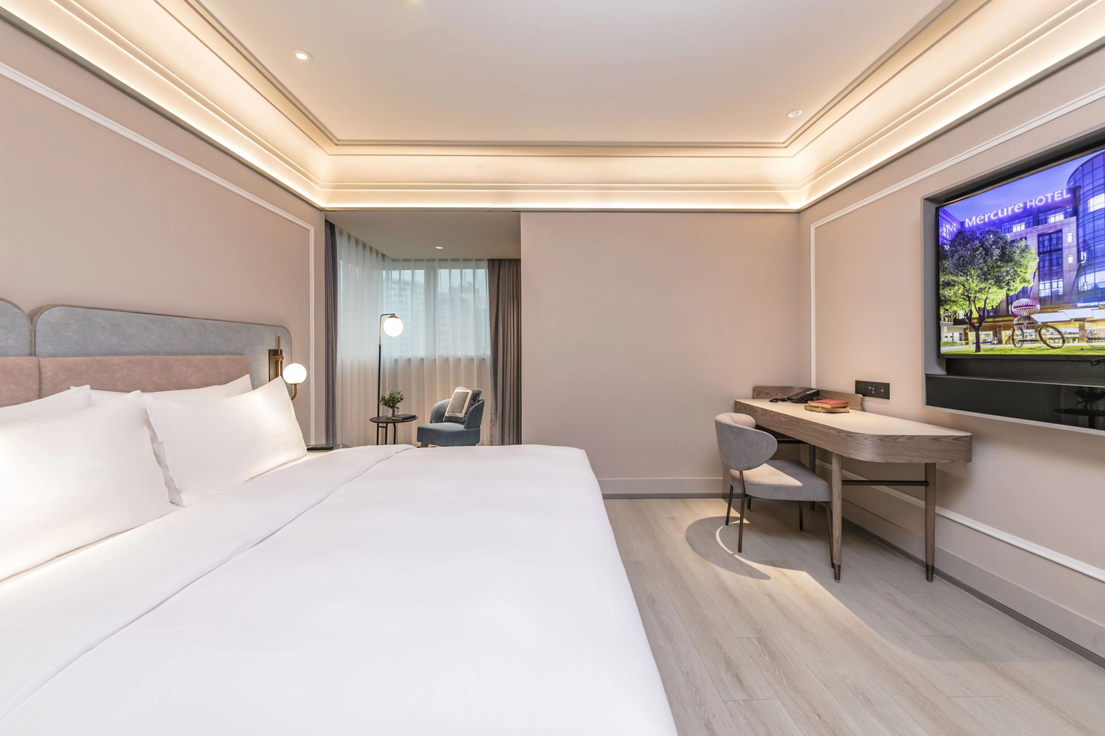 A hotel room with a bed, desk, chair, TV, and a view of the hotel exterior.