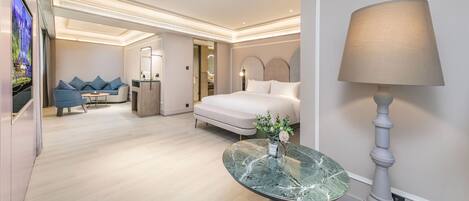 A modern hotel room with a bed, a round table with a vase, a lamp, and a sofa with cushions.