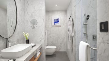 A modern bathroom with a white sink, a mirror, a toilet, and a shower area.