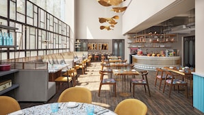 A modern restaurant with a bar area, wooden tables, and chairs, and a large window providing natural light.