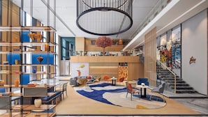 A modern hotel lobby with a central seating area, a staircase, and a large bookshelf.