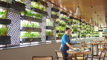 A restaurant with wooden ceiling, hanging plants, and round tables with chairs.