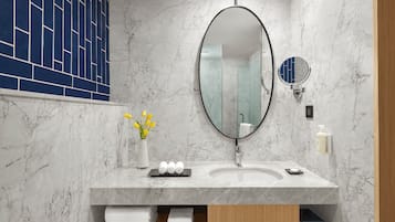 Un baño moderno con un lavabo de mármol, un espejo ovalado grande y un jarrón pequeño con flores amarillas.