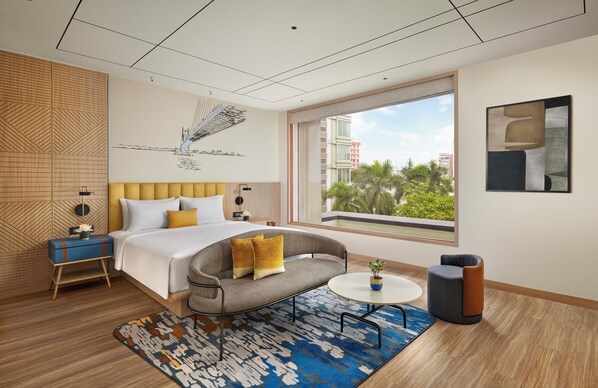 A modern hotel room with a large bed, a sofa, a small table, and a view of palm trees.