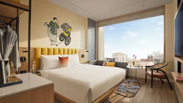 A modern hotel room with a large bed, a sofa, a dining area, and a view of the city.