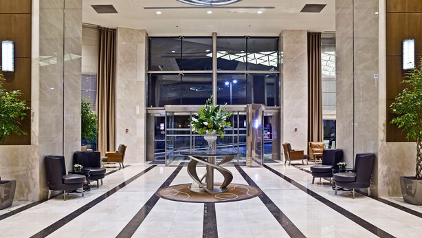 Eine moderne Lobby mit einer zentralen Rezeption, einer Sitzecke und großen Glasüren, die zum Eingang führen.