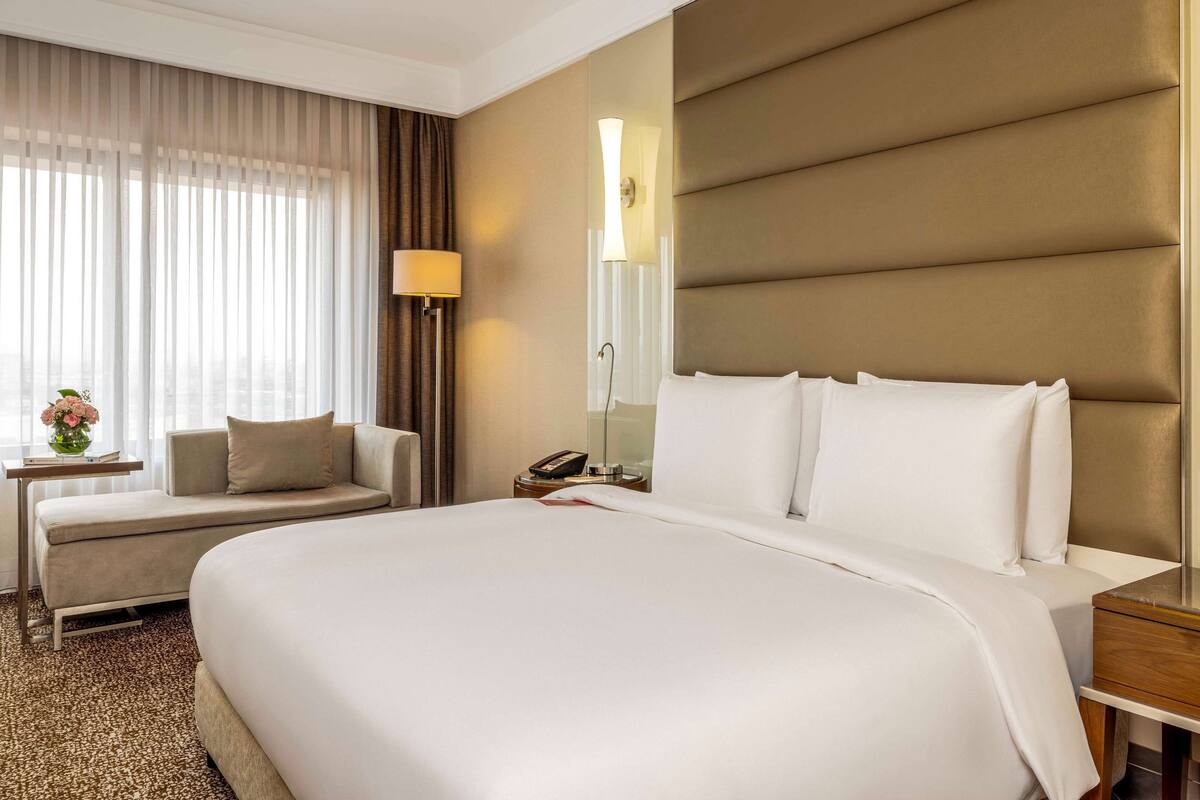 Ein Hotelzimmer mit einem großen Bett, einem Sofa, einem Nachttisch mit Lampe und einem mit Vorhängen versehenen Fenster.