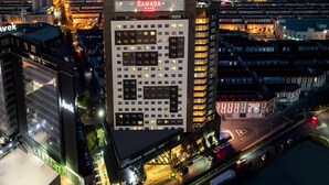 Ein mehrstöckiges Hotel mit einem gut sichtbaren "Ramada Plaza"-Schild, umgeben von anderen Gebäuden und einer belebten Straße.
