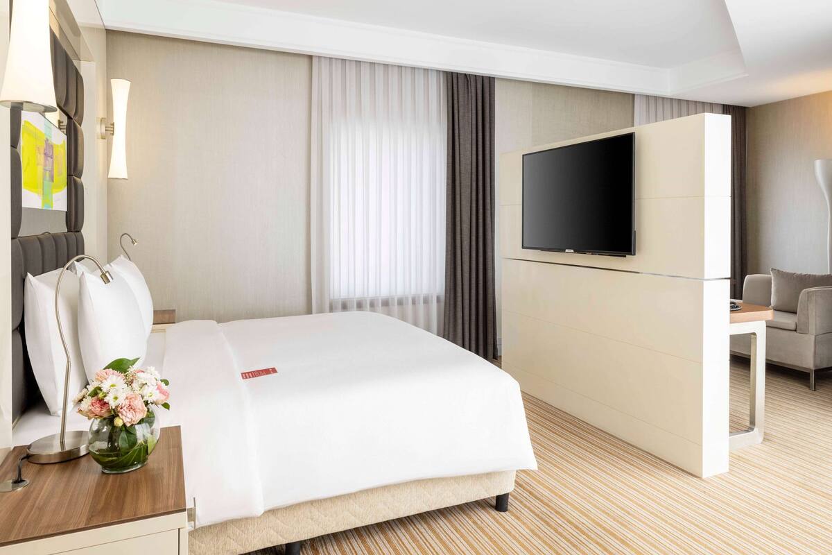 Ein Hotelzimmer mit Bett, Fernseher, Schreibtisch und Blumenvase.