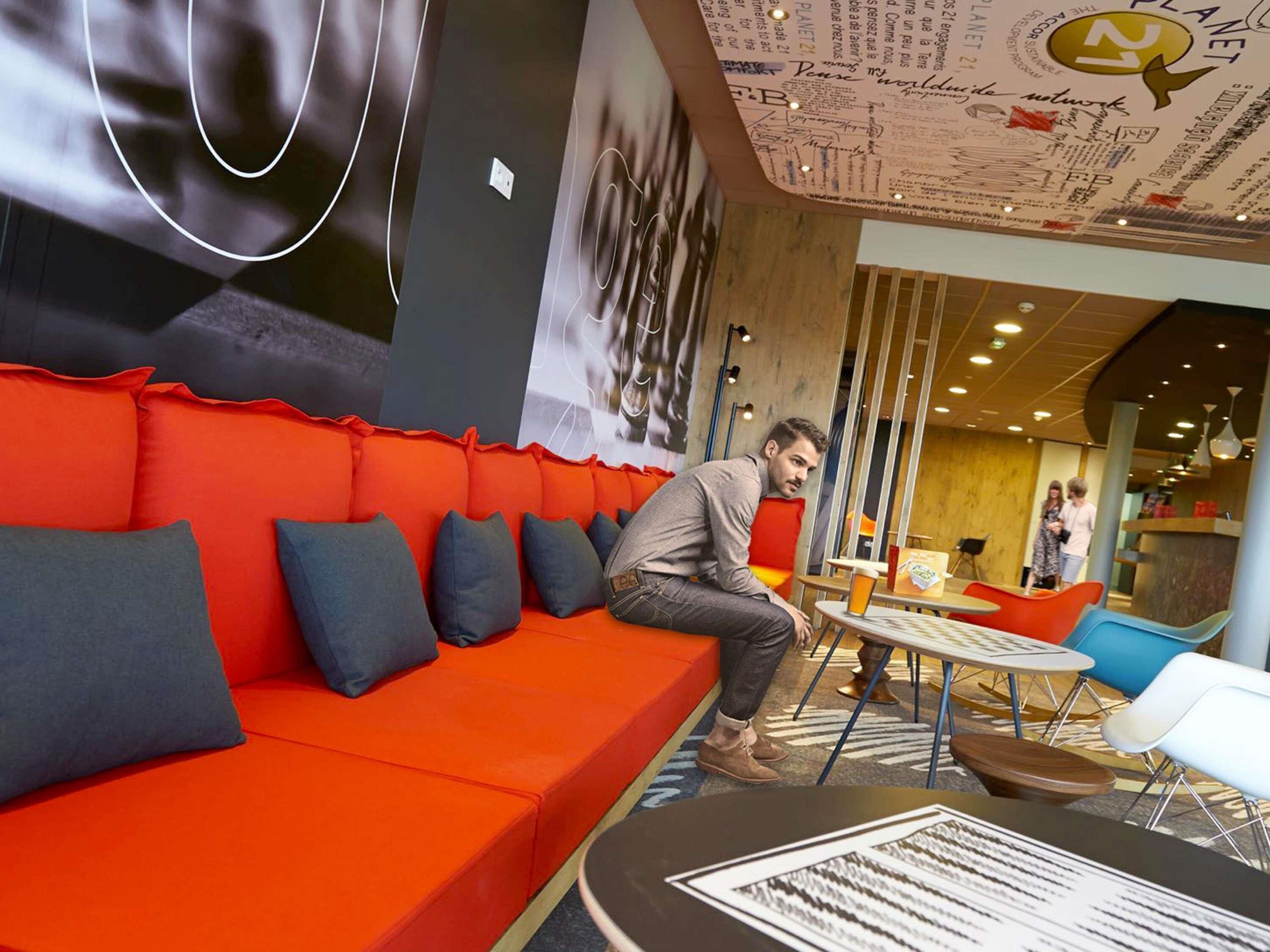 A modern interior with a red sofa, a table with a menu, and a wall with various writings and logos.