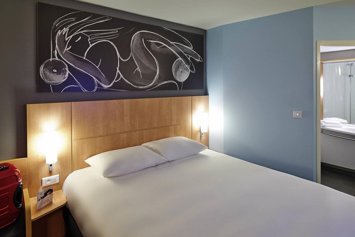 Una habitación de hotel con una cama, lámparas de noche, un cabecero de madera y una obra de arte en la pared.