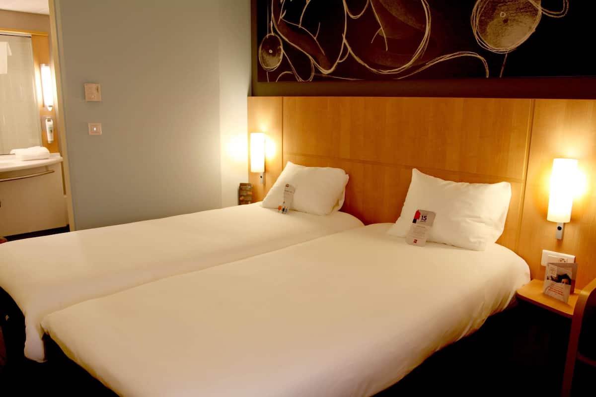 A double bed with white linens, two bedside tables with lamps, and a wooden headboard.