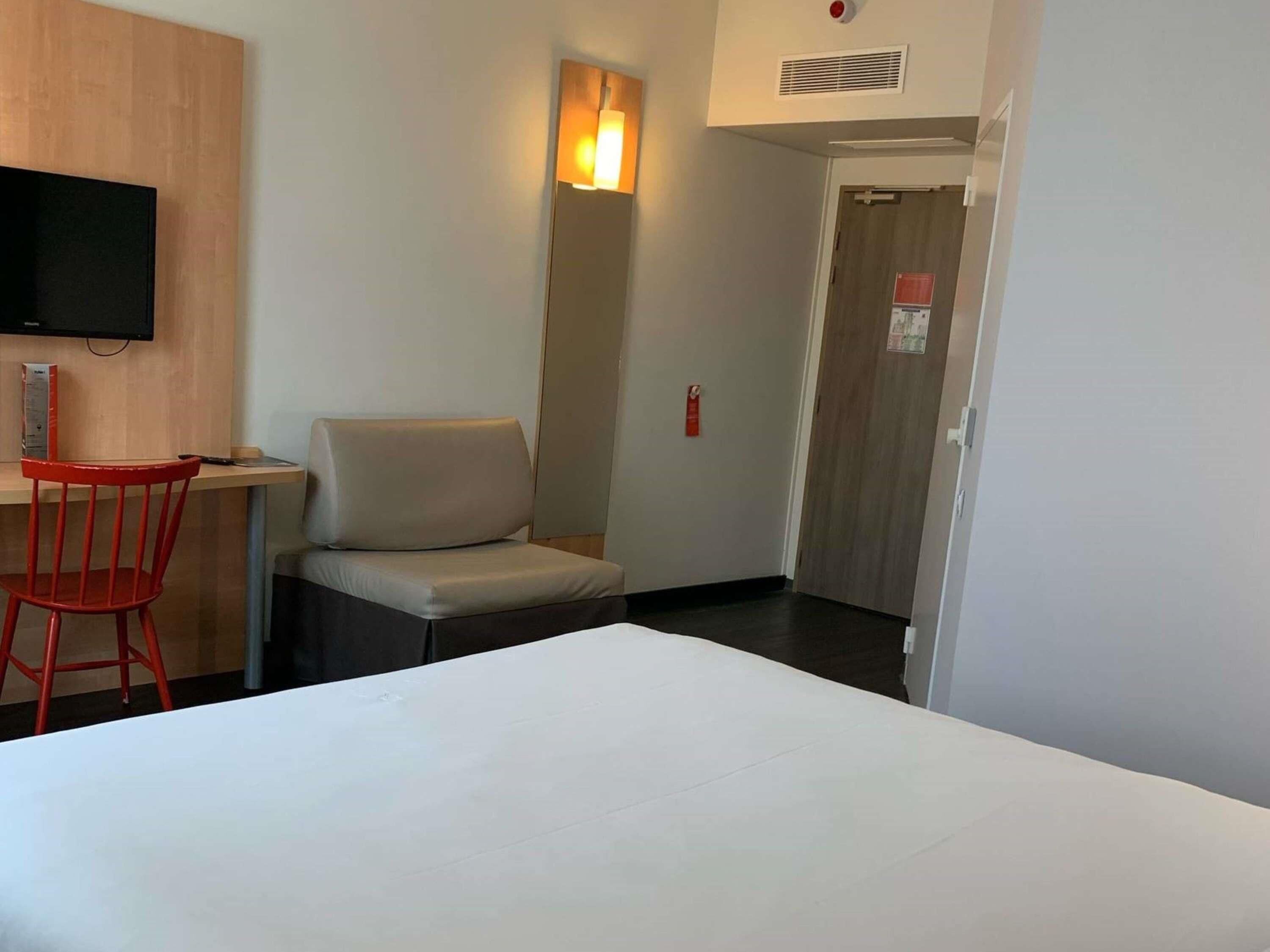 A hotel room with a bed, a desk, a chair, a television, and a door.