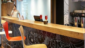 Una zona de bar con mostrador de madera, sillas rojas y una pantalla de proyección al fondo.