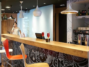 Una zona de bar con mostrador de madera, sillas rojas y una pantalla de proyección al fondo.