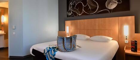 Habitación de hotel con una cama grande, cabecero con iluminación integrada, una obra de arte colgada en la pared y una mesita de noche con lámpara.