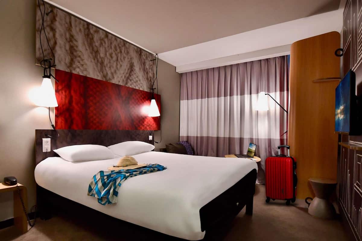 A hotel room with a large bed, a desk, a laptop, a suitcase, and a television.