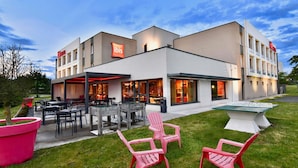 Un hotel moderno con terraza exterior, piscina y césped bien cuidado.