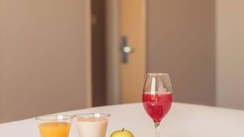 En bakke med morgenmadsprodukter, herunder juice, mælk, en rød drik, en banan, et æble og en sandwich på et hvidt bord.