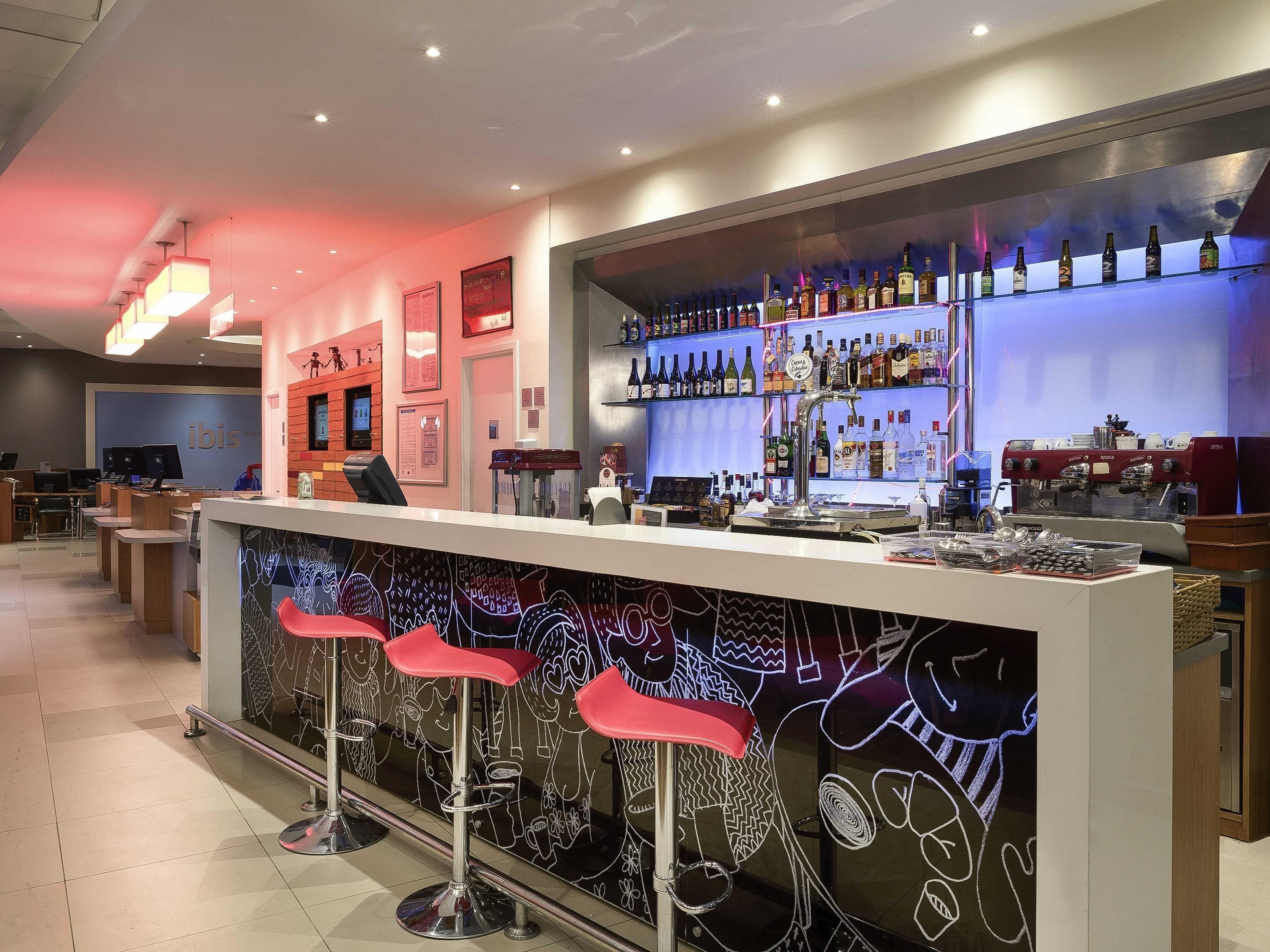 Zona de bar moderna con mostrador, taburetes y una variedad de botellas de licores.