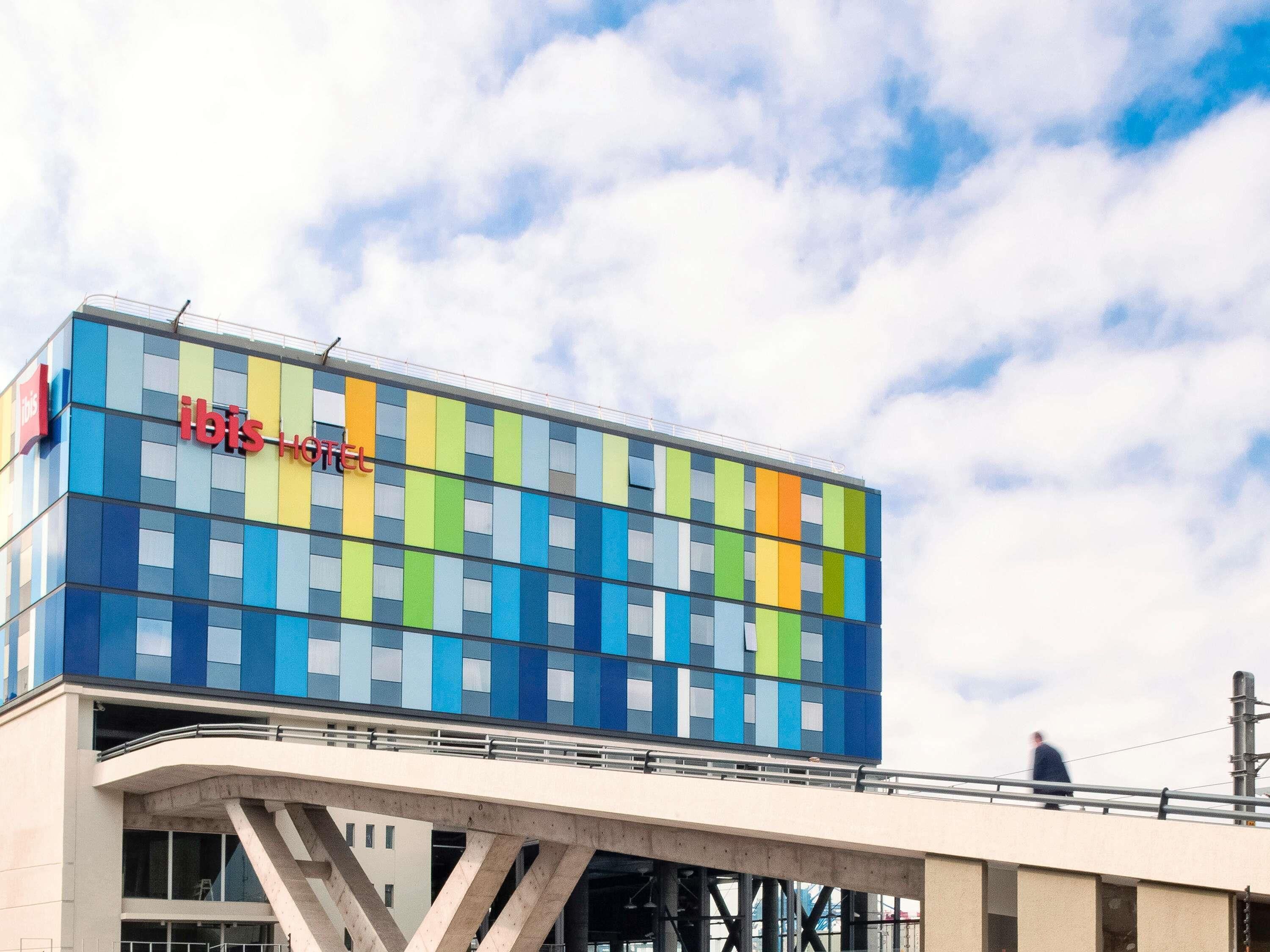 A modern hotel with a colorful facade and a pedestrian bridge.