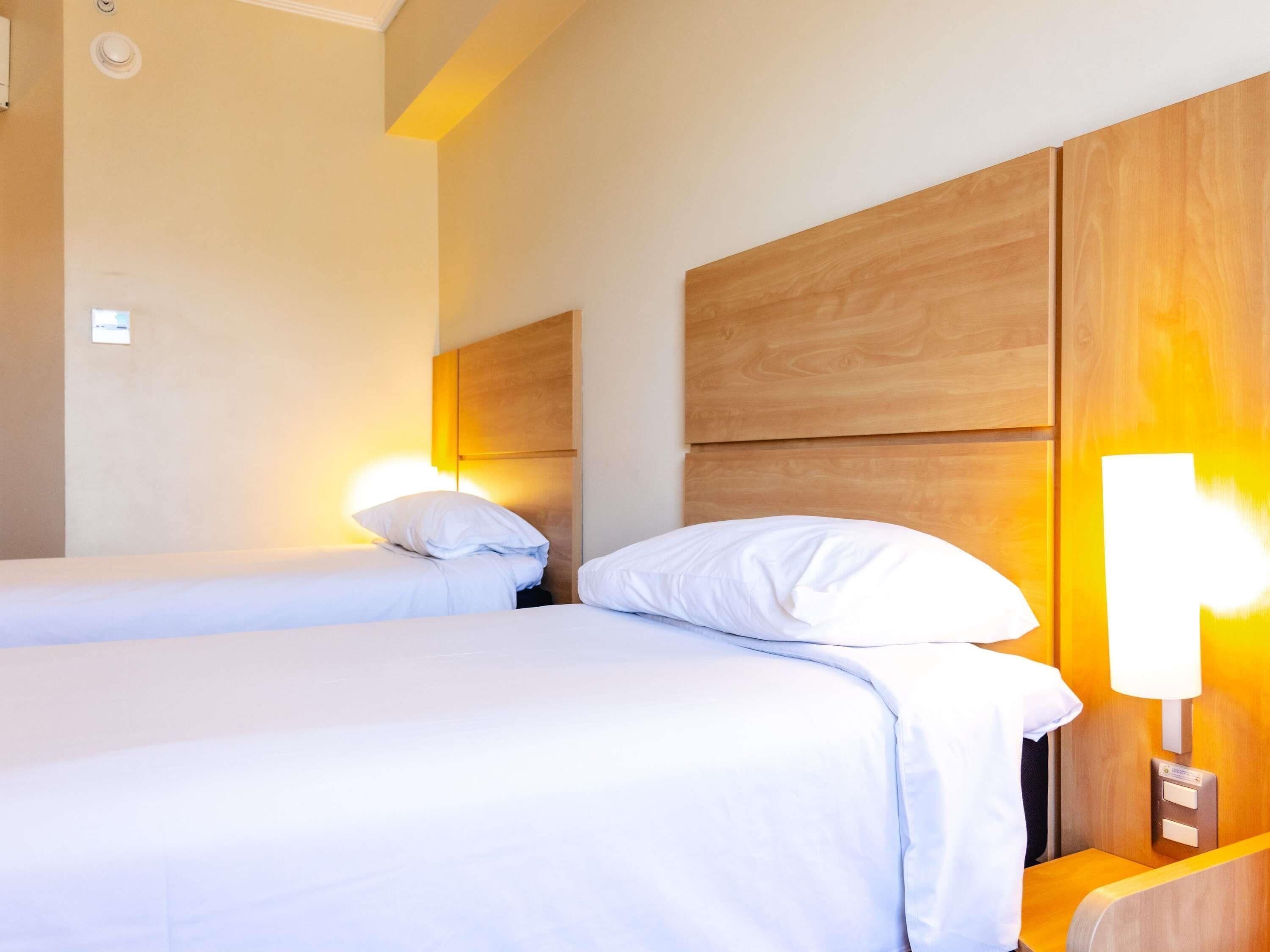 Habitación de hotel con dos camas, cabeceros de madera, lámparas de noche y una mesita.