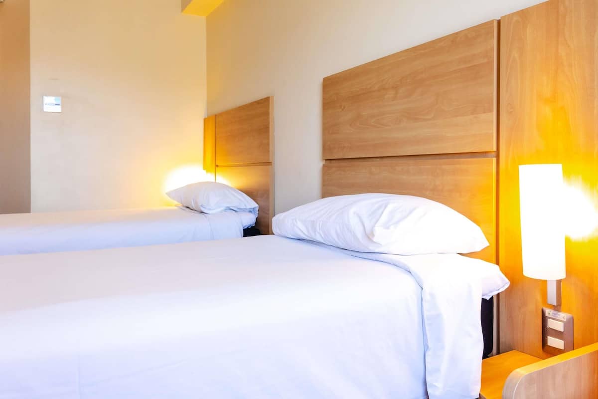 A hotel room with two beds, wooden headboards, bedside lamps, and a small table.