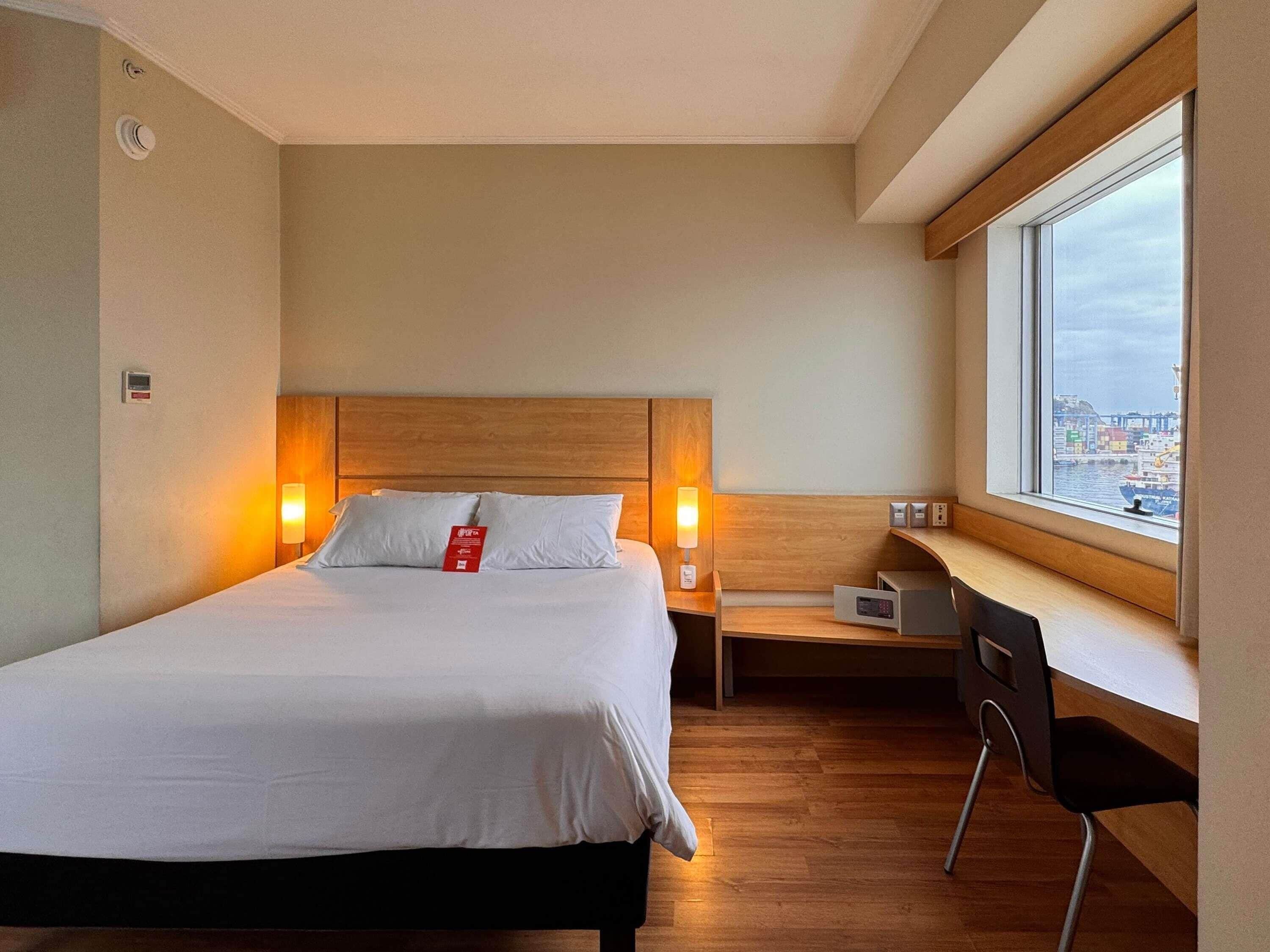Une chambre d’hôtel comprenant un lit, des lampes de chevet, un bureau, une chaise et une fenêtre donnant sur un port.