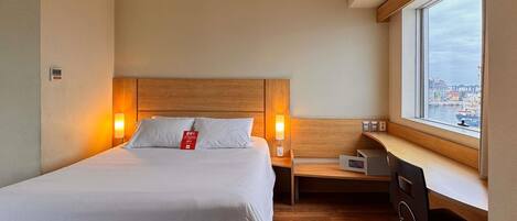 Une chambre d’hôtel comprenant un lit, des lampes de chevet, un bureau, une chaise et une fenêtre donnant sur un port.