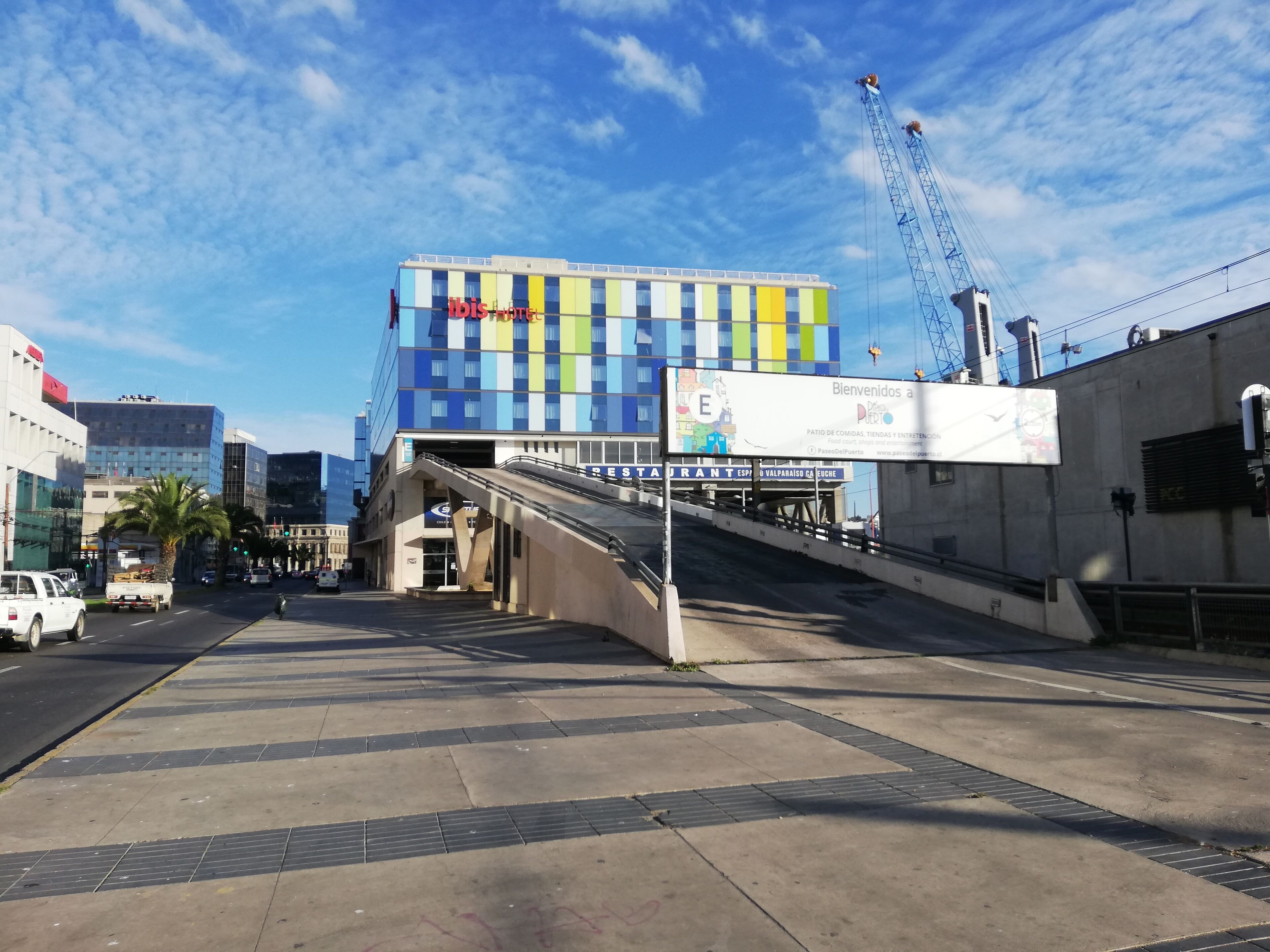 Ein modernes Gebäude mit farbenfroher Fassade, einer Fußgängerbrücke und einer Restaurantwerbetafel.